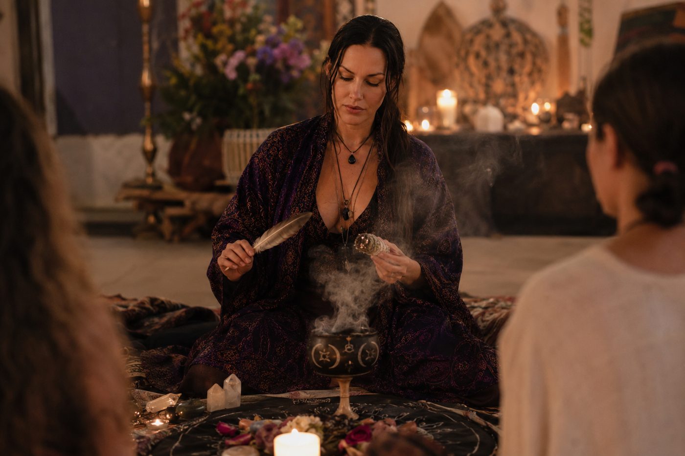 A facilitator leading a candlelit cleansing ritual with sage smoke and a feather, guests seated in a sacred circle